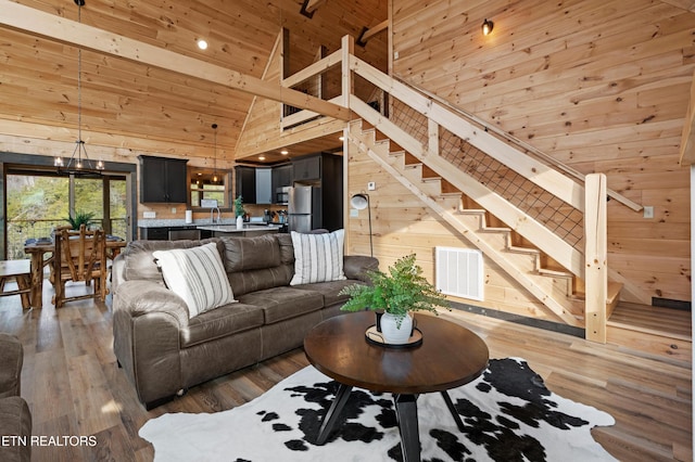 living room featuring high vaulted ceiling, wood walls, wooden ceiling, visible vents, and stairway