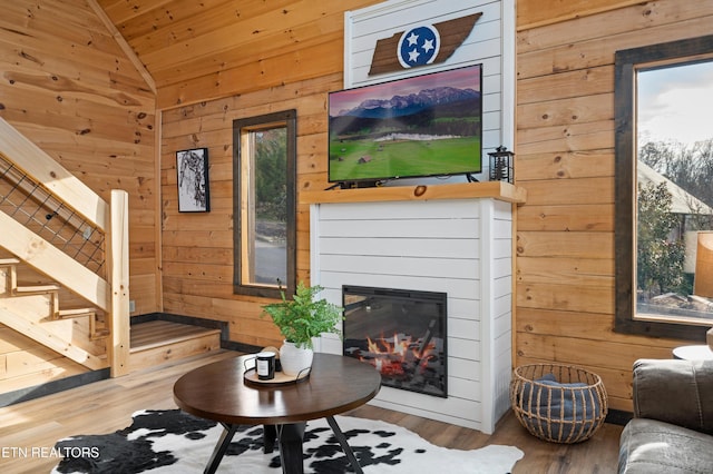 living area featuring vaulted ceiling, wood walls, wood finished floors, wooden ceiling, and stairs
