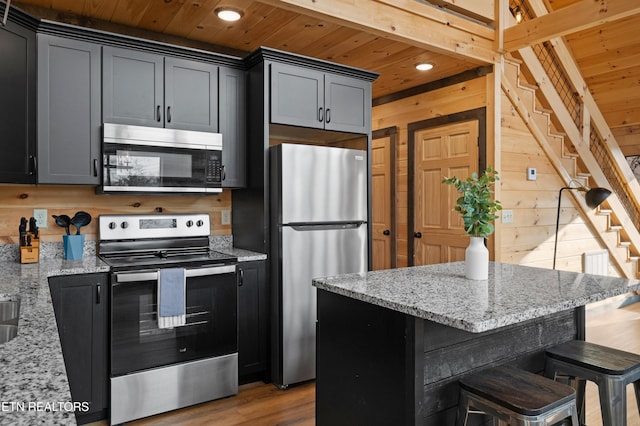 kitchen featuring light stone counters, wood walls, wood ceiling, and stainless steel appliances