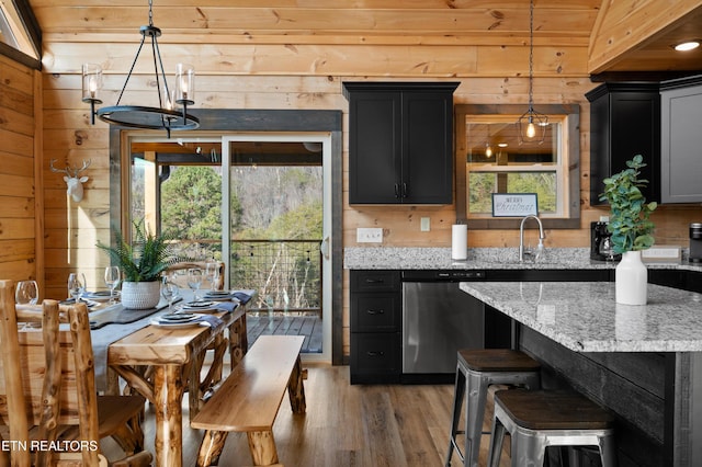 kitchen featuring dark cabinets, stainless steel dishwasher, wood walls, and light wood-style flooring