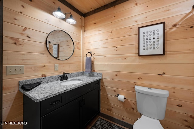 half bath with wooden walls, toilet, wood ceiling, and vanity