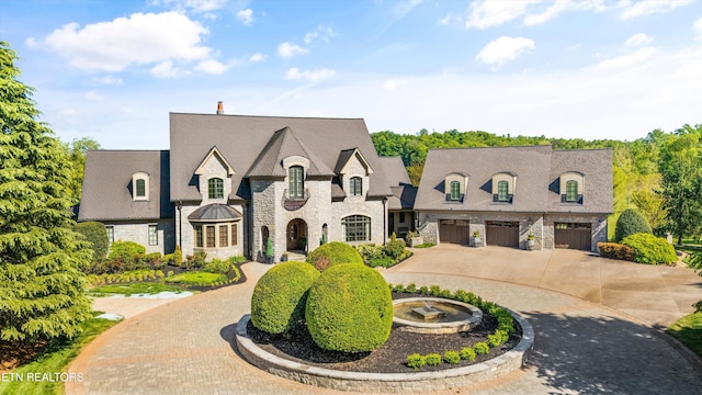 french country home featuring curved driveway, an attached garage, and stone siding