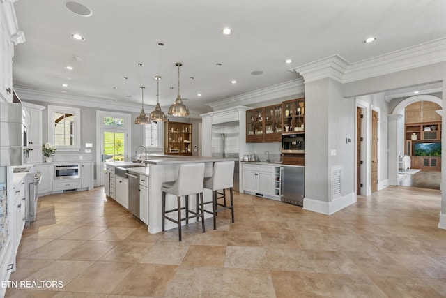 kitchen with a kitchen bar, a large island with sink, a sink, glass insert cabinets, and stainless steel appliances