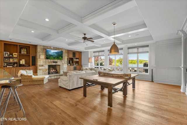living area with light wood-type flooring, a ceiling fan, coffered ceiling, and a fireplace