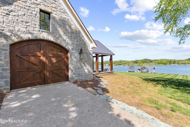 entrance to property featuring a lawn, a water view, and stone siding