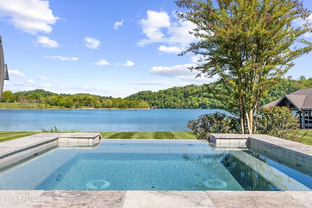 outdoor pool with a view of trees, a water view, and an in ground hot tub