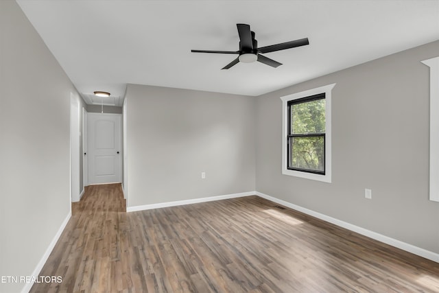 unfurnished room with a ceiling fan, baseboards, wood finished floors, and attic access