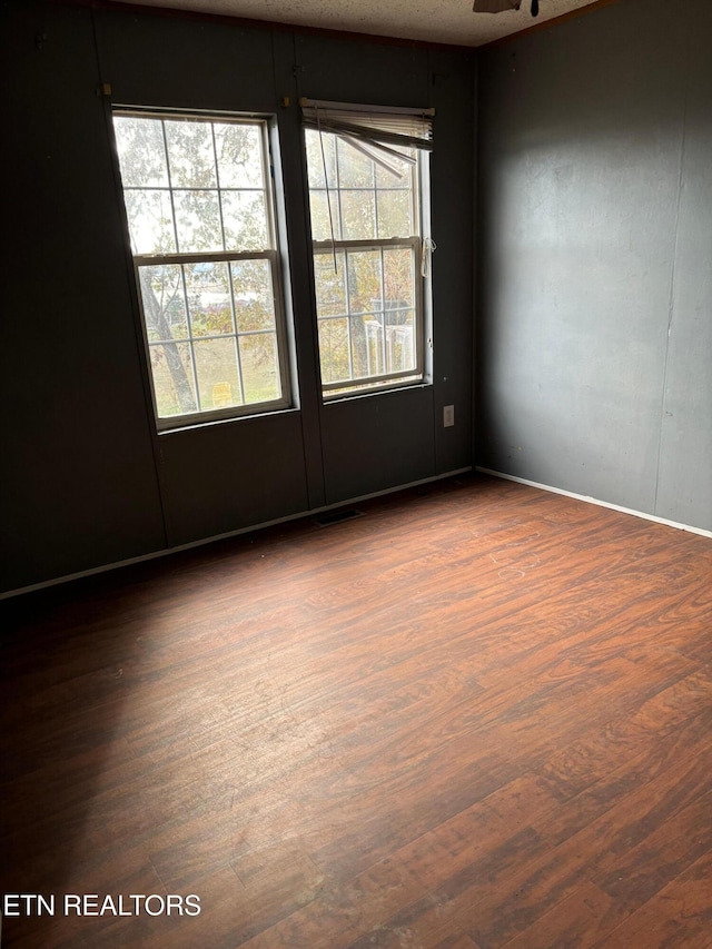 empty room with dark wood-type flooring, a ceiling fan, and visible vents