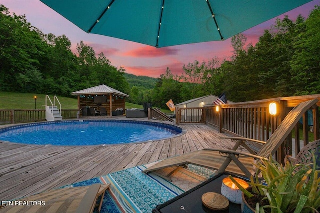 pool at dusk with a gazebo, an outdoor hangout area, an outdoor pool, and a deck