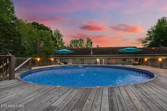 pool at dusk with a deck and an outdoor pool
