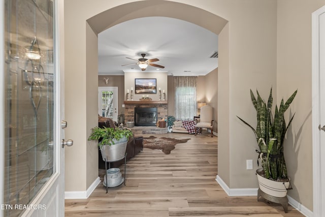 living room with a fireplace, baseboards, arched walkways, a ceiling fan, and light wood-style flooring