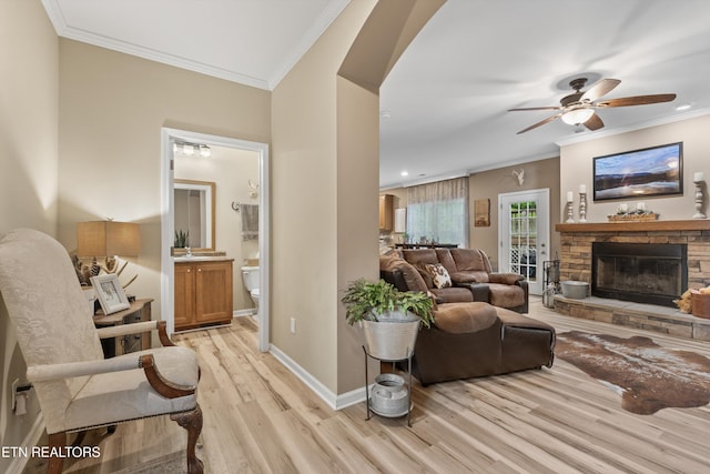 living area with light wood-type flooring, ornamental molding, a ceiling fan, and a fireplace