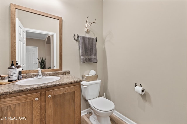 half bathroom with vanity, baseboards, toilet, and wood finished floors