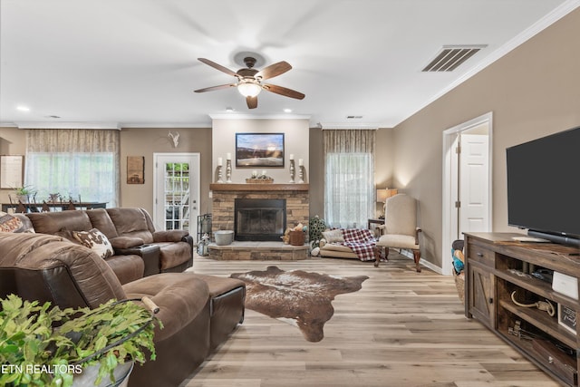 living room featuring crown molding, a stone fireplace, a ceiling fan, light wood-type flooring, and visible vents