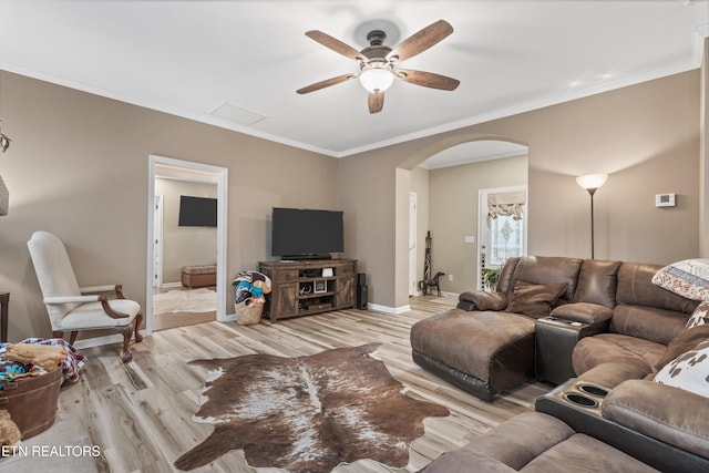 living area featuring a ceiling fan, visible vents, arched walkways, light wood-type flooring, and ornamental molding