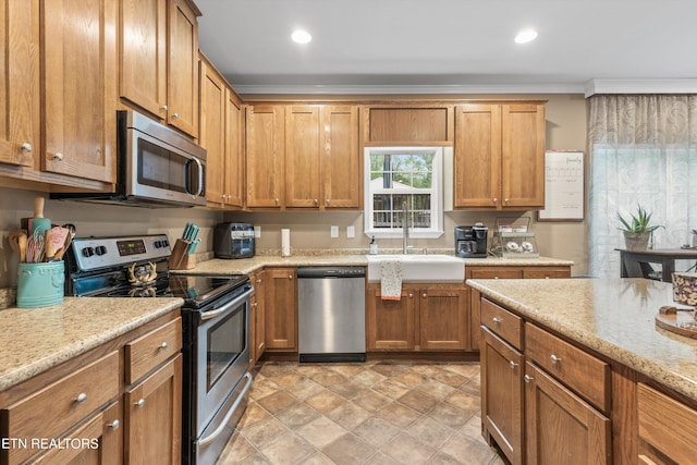 kitchen with brown cabinetry, ornamental molding, a sink, stone finish flooring, and stainless steel appliances
