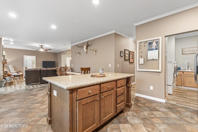 kitchen featuring ornamental molding, washer and dryer, baseboards, a ceiling fan, and stone finish flooring