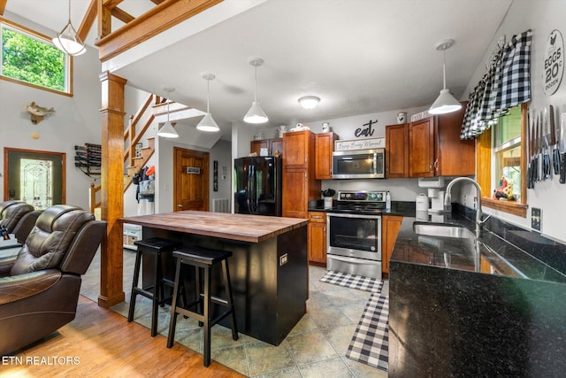 kitchen with butcher block countertops, open floor plan, brown cabinets, a sink, and stainless steel appliances