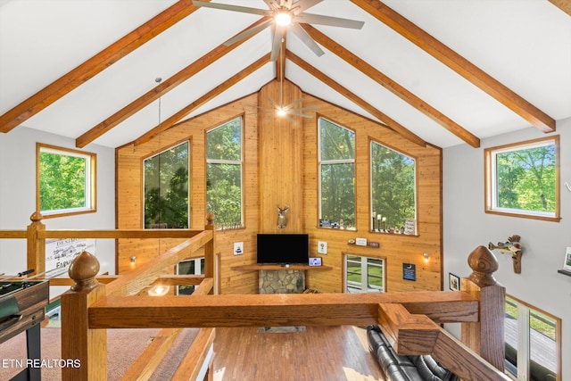 living room featuring lofted ceiling with beams, a ceiling fan, wood walls, and a wealth of natural light