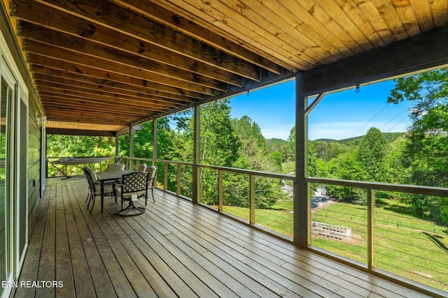 wooden deck with a lawn, outdoor dining space, and a forest view