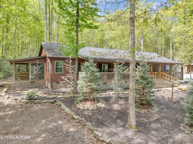 view of front of house featuring a shingled roof, a sunroom, crawl space, a view of trees, and covered porch