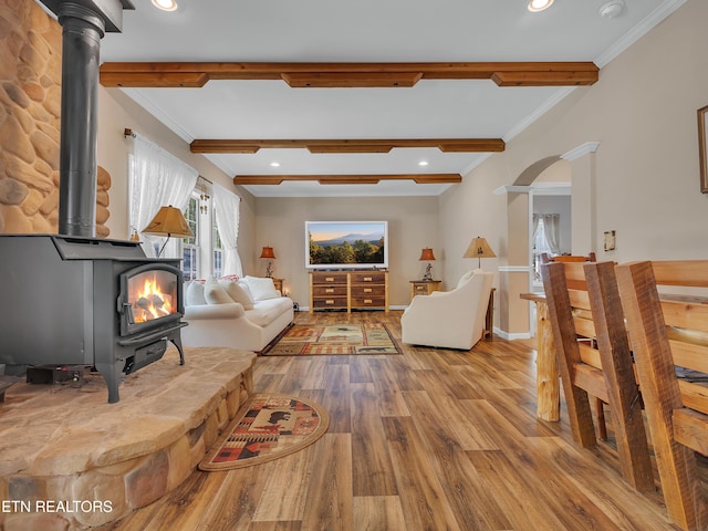 living area with crown molding, beamed ceiling, a wood stove, and wood finished floors