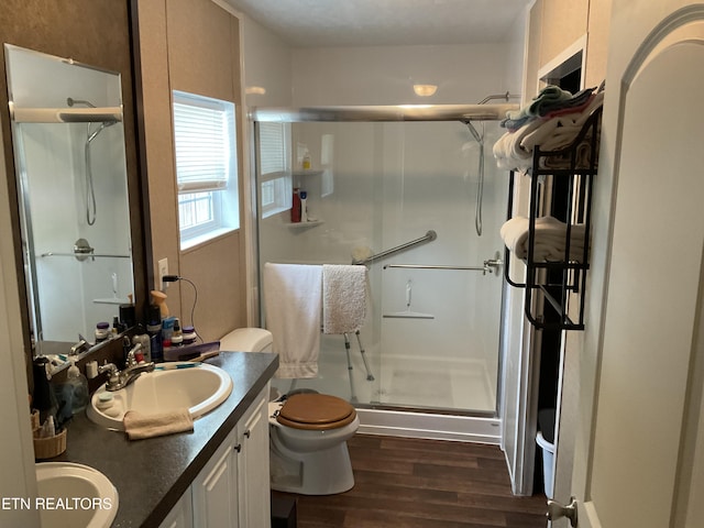 full bathroom featuring double vanity, wood finished floors, toilet, a shower stall, and a sink
