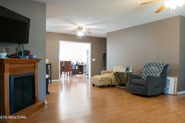 living room featuring a fireplace, a ceiling fan, and light wood-type flooring
