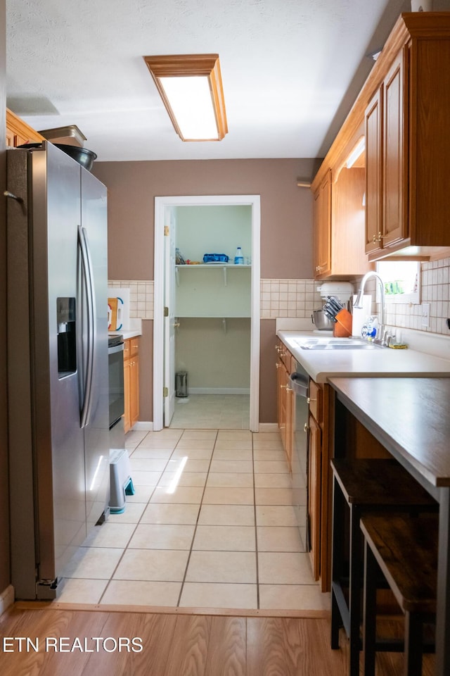 kitchen with brown cabinetry, decorative backsplash, a sink, light tile patterned floors, and stainless steel appliances