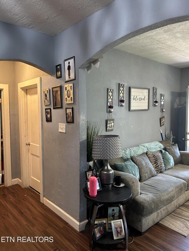 living room with arched walkways, a textured ceiling, dark wood-style floors, and baseboards