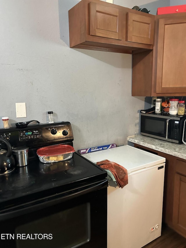 kitchen with light countertops, stainless steel microwave, black electric range oven, and brown cabinets