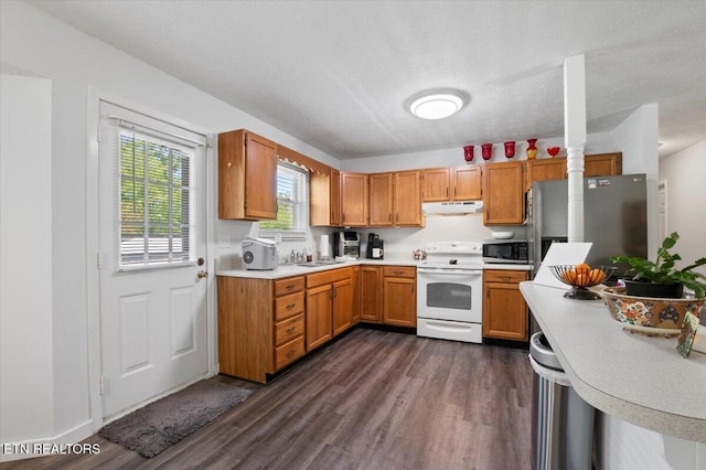 kitchen with appliances with stainless steel finishes, a sink, light countertops, dark wood finished floors, and under cabinet range hood