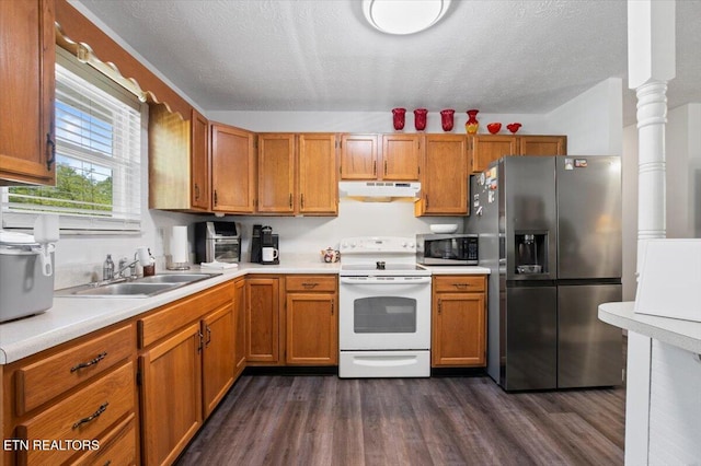 kitchen with appliances with stainless steel finishes, a sink, light countertops, under cabinet range hood, and dark wood-type flooring