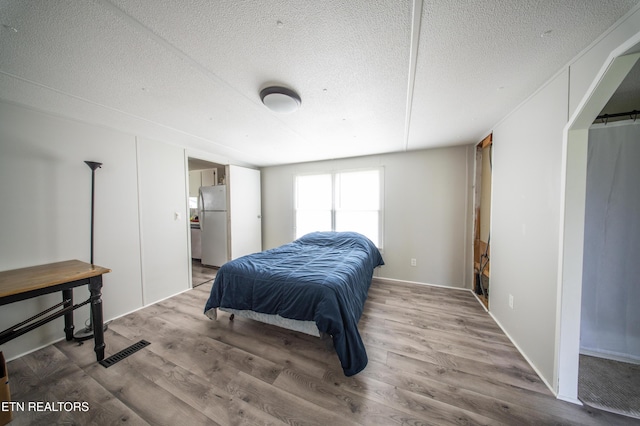 bedroom with visible vents, freestanding refrigerator, a textured ceiling, and wood finished floors