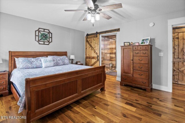 bedroom with ceiling fan, a barn door, and dark wood-type flooring