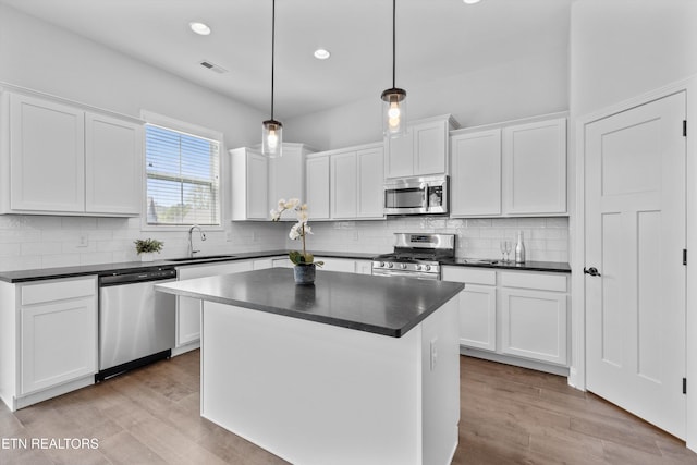 kitchen featuring visible vents, wood finished floors, dark countertops, a sink, and appliances with stainless steel finishes