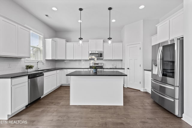 kitchen with dark countertops, a center island, white cabinets, a sink, and stainless steel appliances