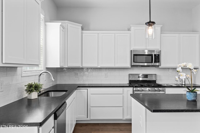 kitchen with dark countertops, white cabinetry, a sink, dark wood finished floors, and stainless steel appliances