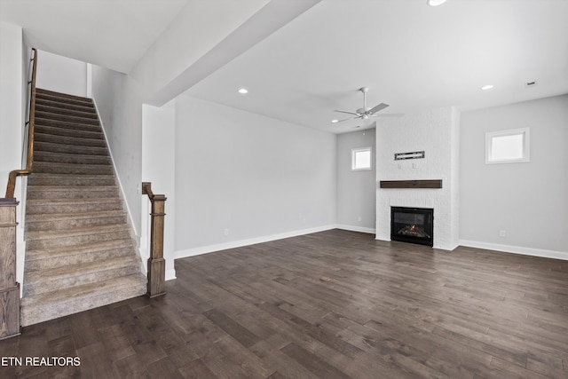 unfurnished living room featuring dark wood-style flooring, stairs, ceiling fan, and a large fireplace