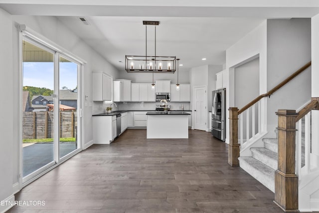 kitchen featuring dark countertops, dark wood-style floors, a center island, a chandelier, and appliances with stainless steel finishes
