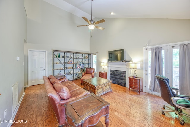 living area with a ceiling fan, visible vents, wood finished floors, high vaulted ceiling, and a glass covered fireplace