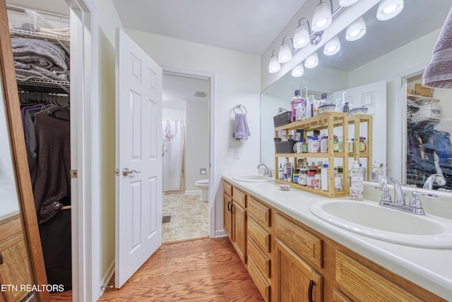bathroom featuring a sink, double vanity, toilet, and wood finished floors