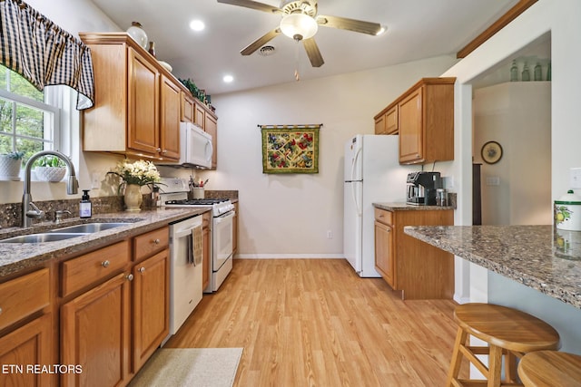 kitchen with brown cabinetry, a ceiling fan, a sink, light wood finished floors, and white appliances
