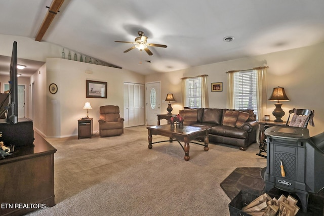 carpeted living area featuring vaulted ceiling with beams, a wood stove, ceiling fan, and visible vents