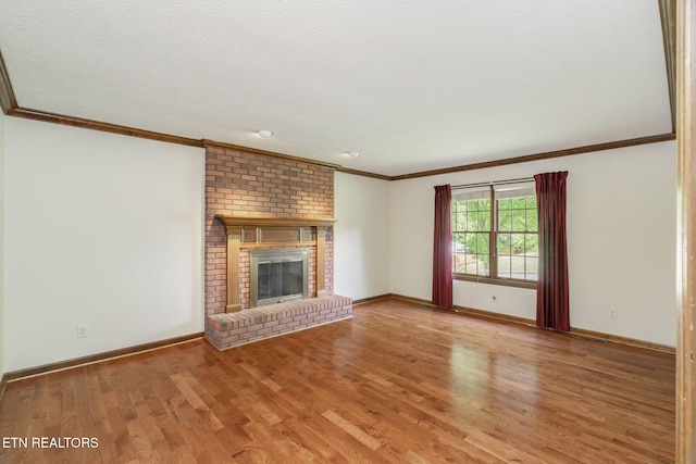unfurnished living room with crown molding, visible vents, a brick fireplace, wood finished floors, and baseboards