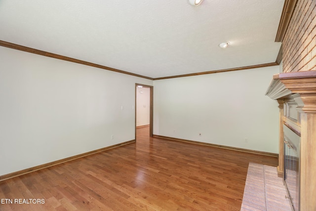 unfurnished living room with light wood-style floors, ornamental molding, baseboards, and a brick fireplace