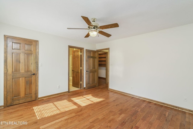 unfurnished bedroom featuring a ceiling fan, baseboards, a spacious closet, and light wood-style floors