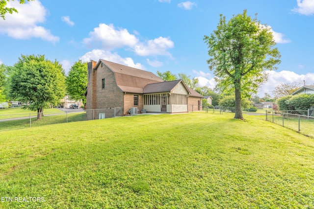 back of house with a lawn, a chimney, a fenced backyard, and a sunroom