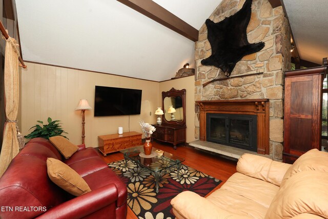 living area featuring a stone fireplace, lofted ceiling with beams, and wood finished floors