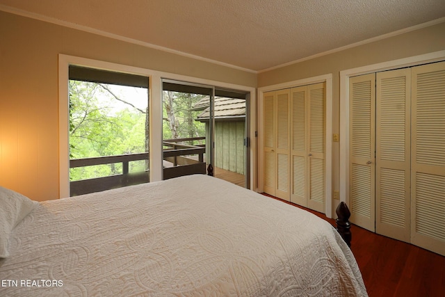 bedroom with two closets, a textured ceiling, ornamental molding, and wood finished floors